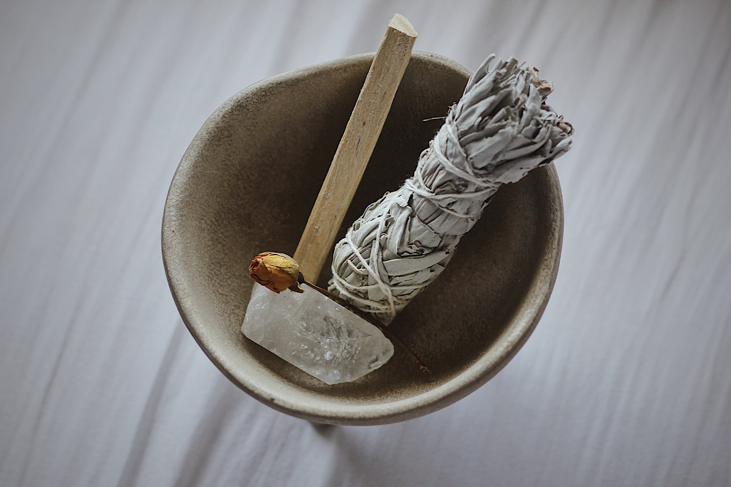 grey clay bowl with palo santo, a dried flower, sage and crystal